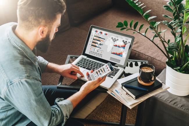 Man casually dressed sat down with a computer and mobile phone, drinking coffee